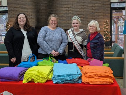 Sarah Miles, Jennifer Davis, Penelope Murphy, and Lauren Jarroll standing behind a table filled with colorful blankets. The table has the red Save the Children banner on it.