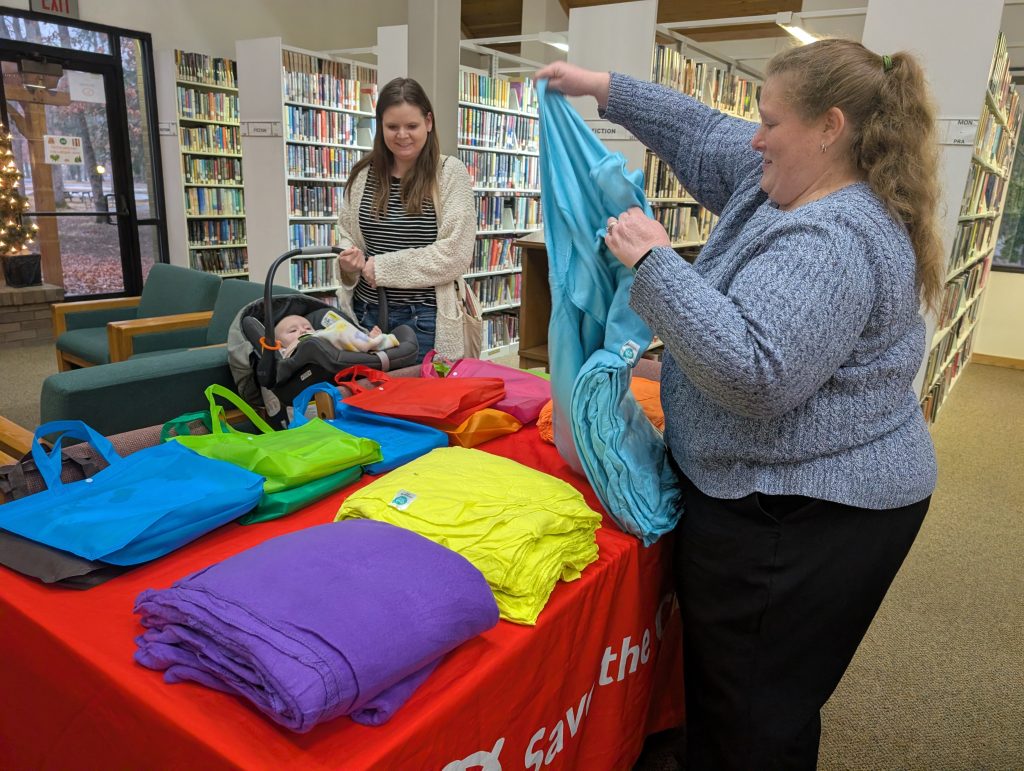 Jennifer Davis reaches a blue blanket to Donna Miller who holds her infant son in a baby carrier.