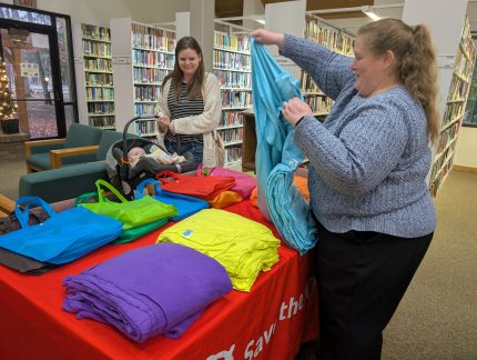 Jennifer Davis reaches a blue blanket to Donna Miller who holds her infant son in a baby carrier.